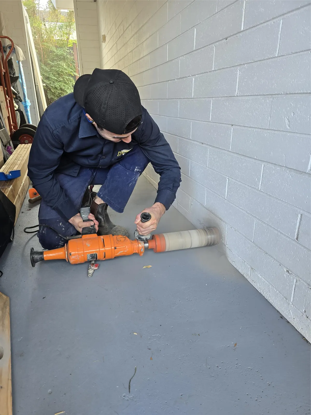 Protech technician core-drilling a brick wall for a subfloor vent in Mentone