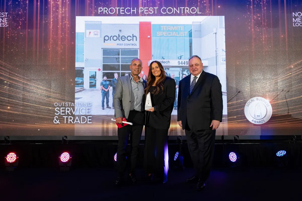 Muzi Tsolakis and Reiannan Nikolaidis accepting the Outstanding Service and Trade award on stage, the screen behind showing the category
